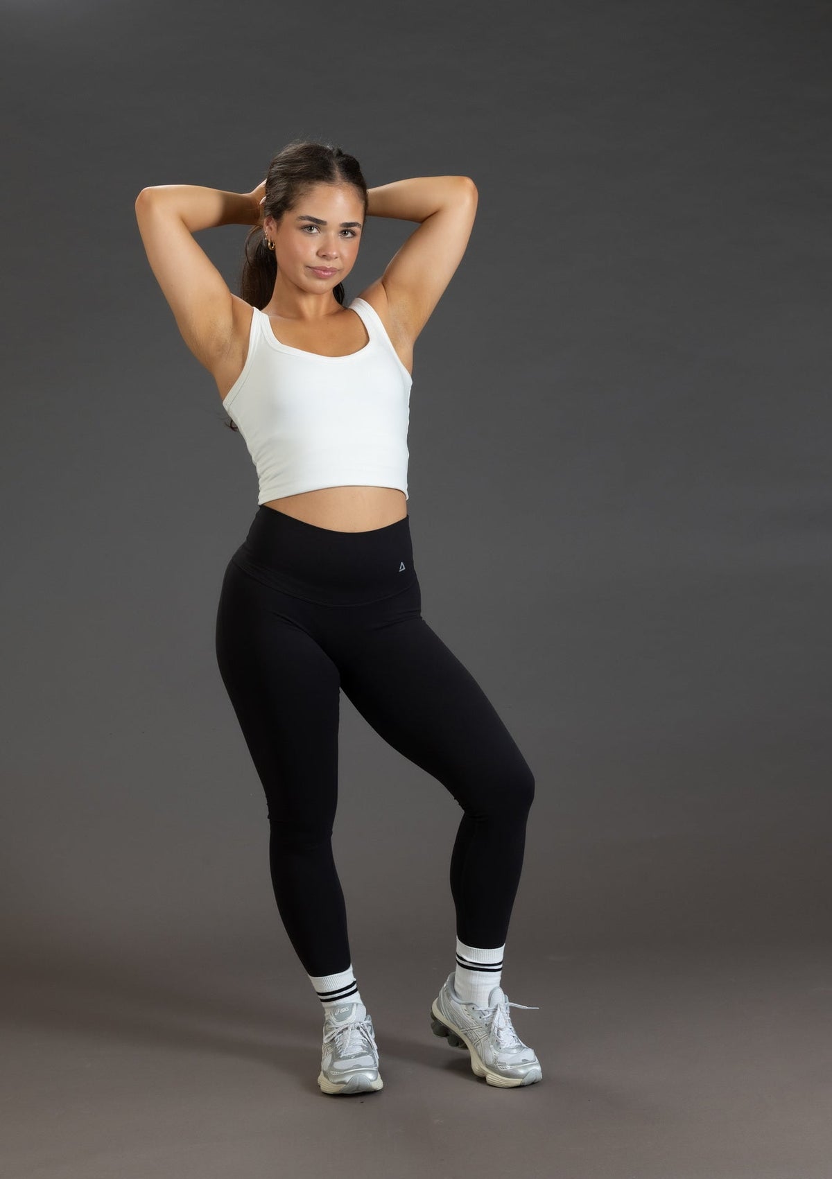 Woman in white crop top and black leggings posing against a gray background